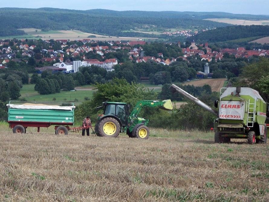 Mithilfe bei der Ernte! Mähdrescher fahren mit herrlichem Blick auf Ostheim vor der Rhön.